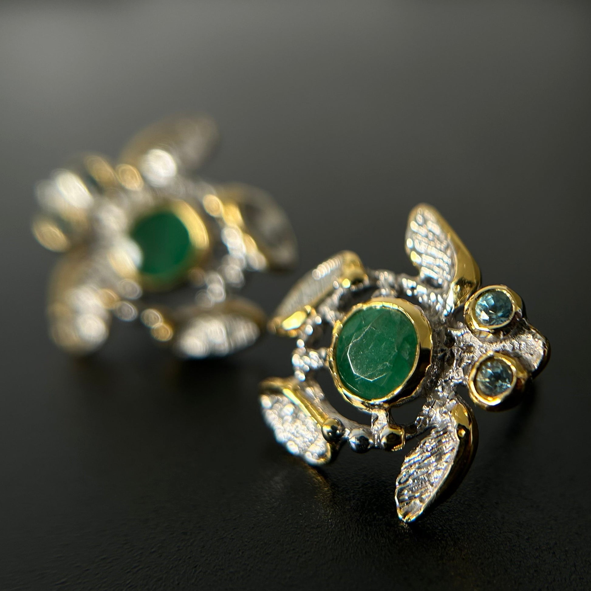 Gold silver turtle-shaped earrings with green emerald stones on a black background