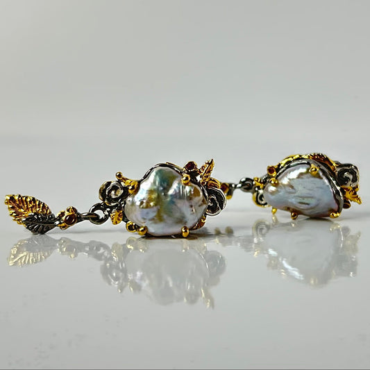 Pair of pearl earrings with gold accents on a reflective surface.