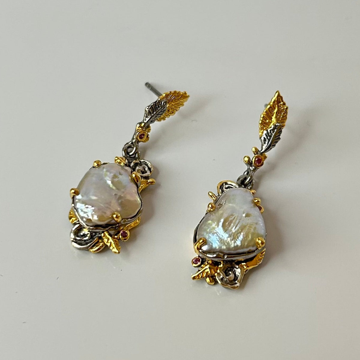 Pair of gold and silver earrings with teardrop-shaped pearls on a light gray background