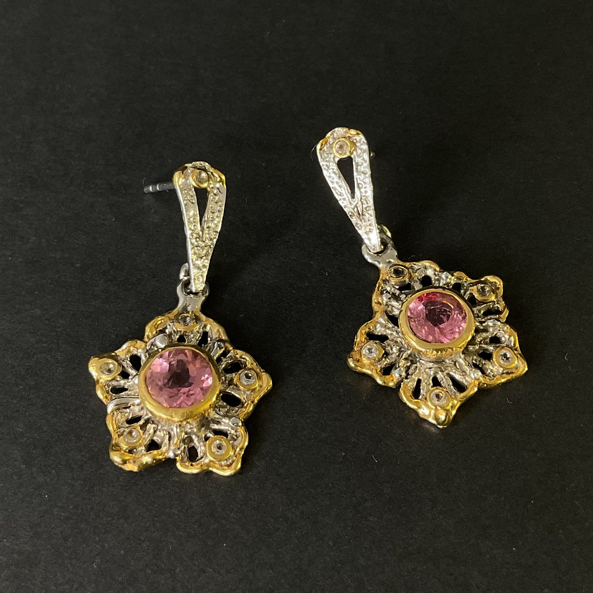 Pair of gold and silver earrings with pink gemstones on a black background