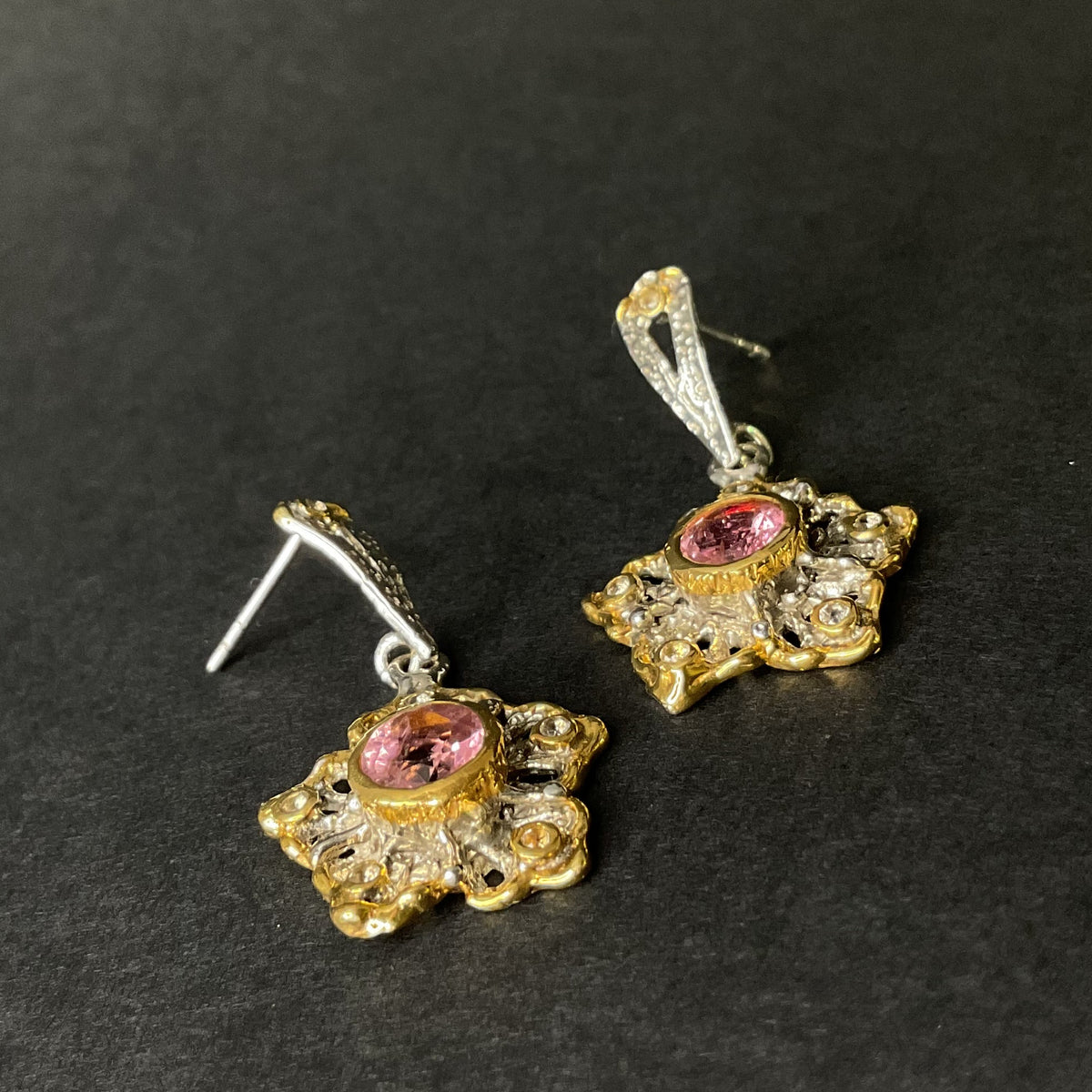 Pair of gold and silver earrings with pink gemstones on a black background