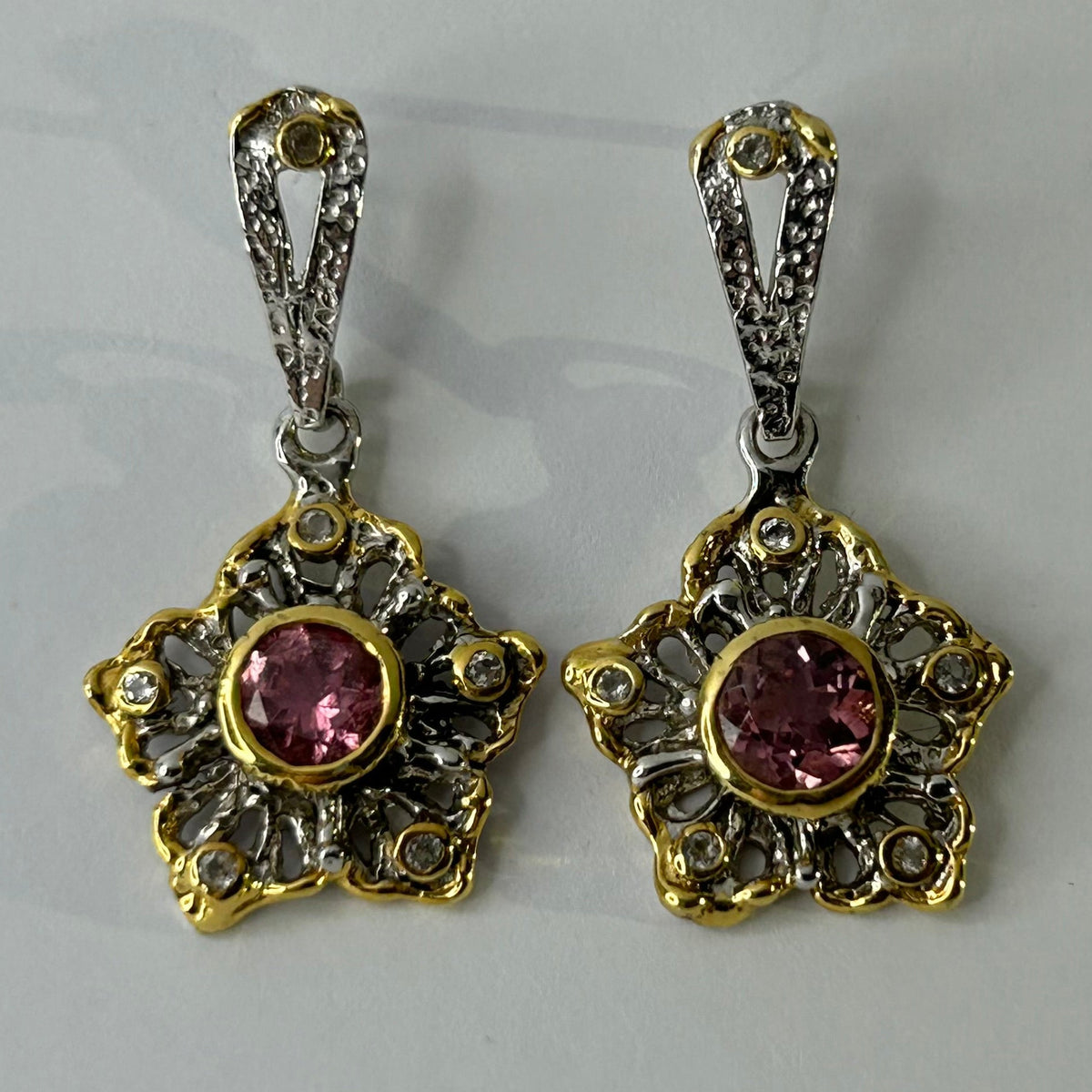 Pair of ornate earrings with pink gemstones on a light gray background