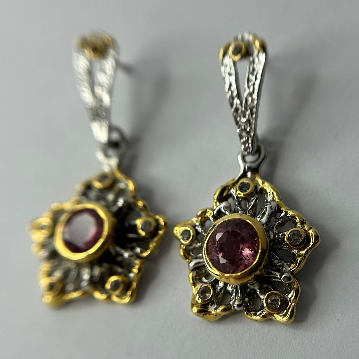 Pair of ornate silver earrings with tourmaline gemstones on a gray background
