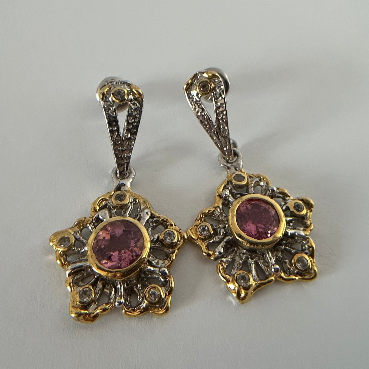 Pair of gold and silver earrings with pink gemstones on a gray background
