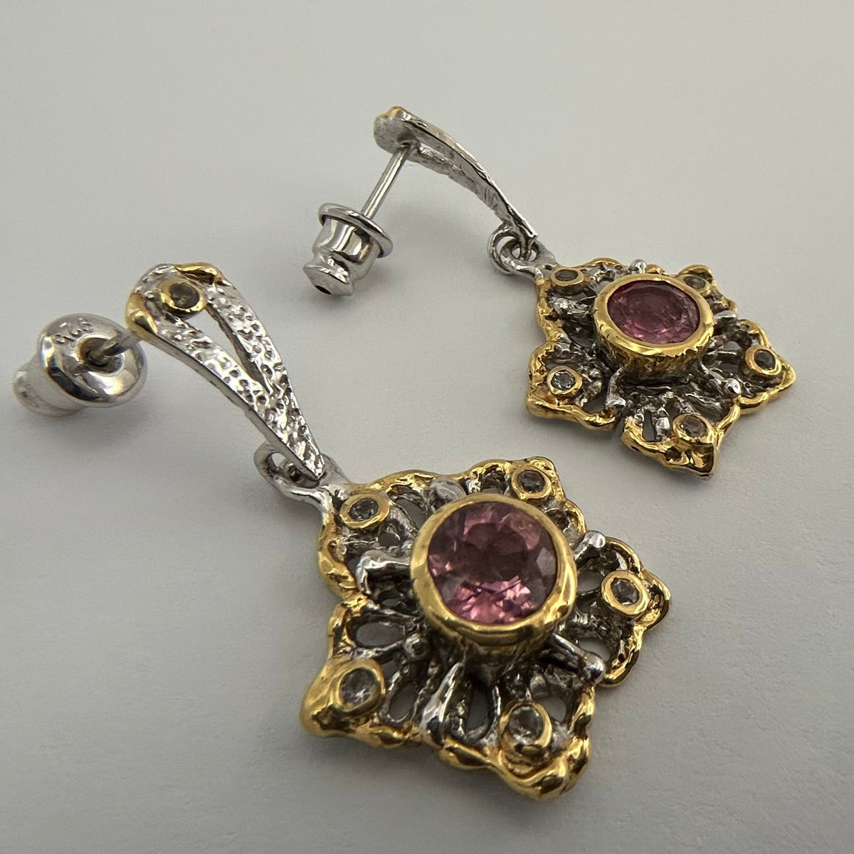Pair of ornate earrings with tourmaline gemstones on a gray background