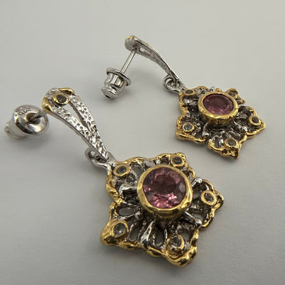 Pair of ornate earrings with tourmaline gemstones on a gray background