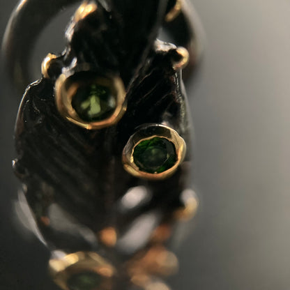 Close-up of a black and gold earring with green gemstones on a dark background