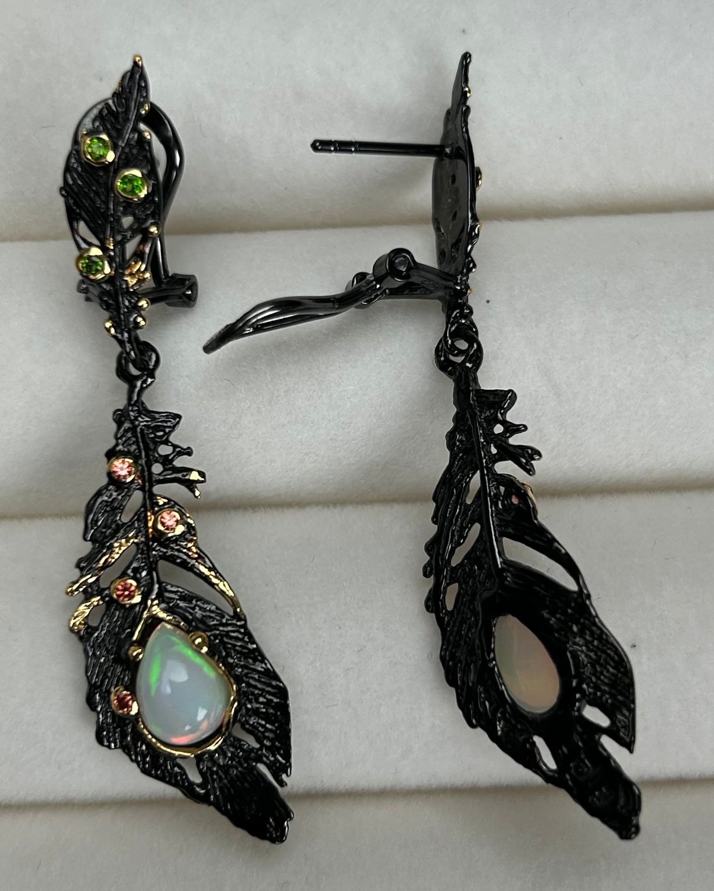 Ornate black feather earrings with a central gemstone on a white background