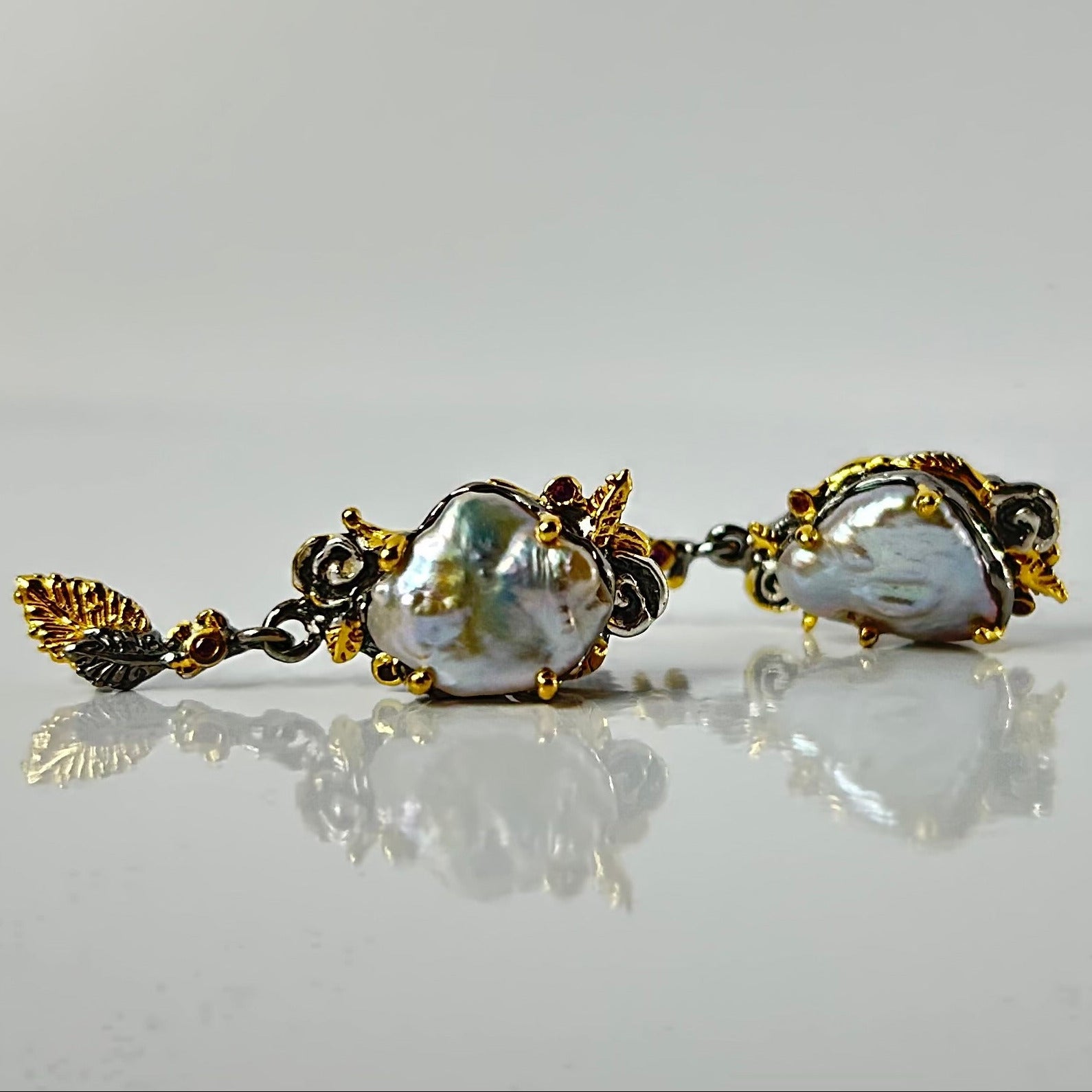 Pair of pearl earrings with gold accents on a reflective surface.