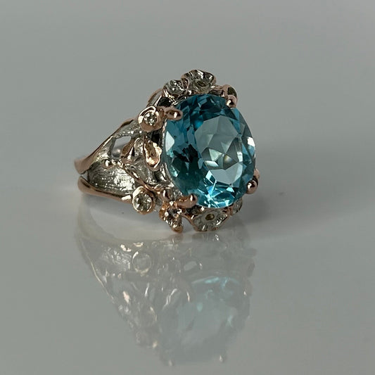 Silver ring with a blue topaz gemstone on a reflective surface