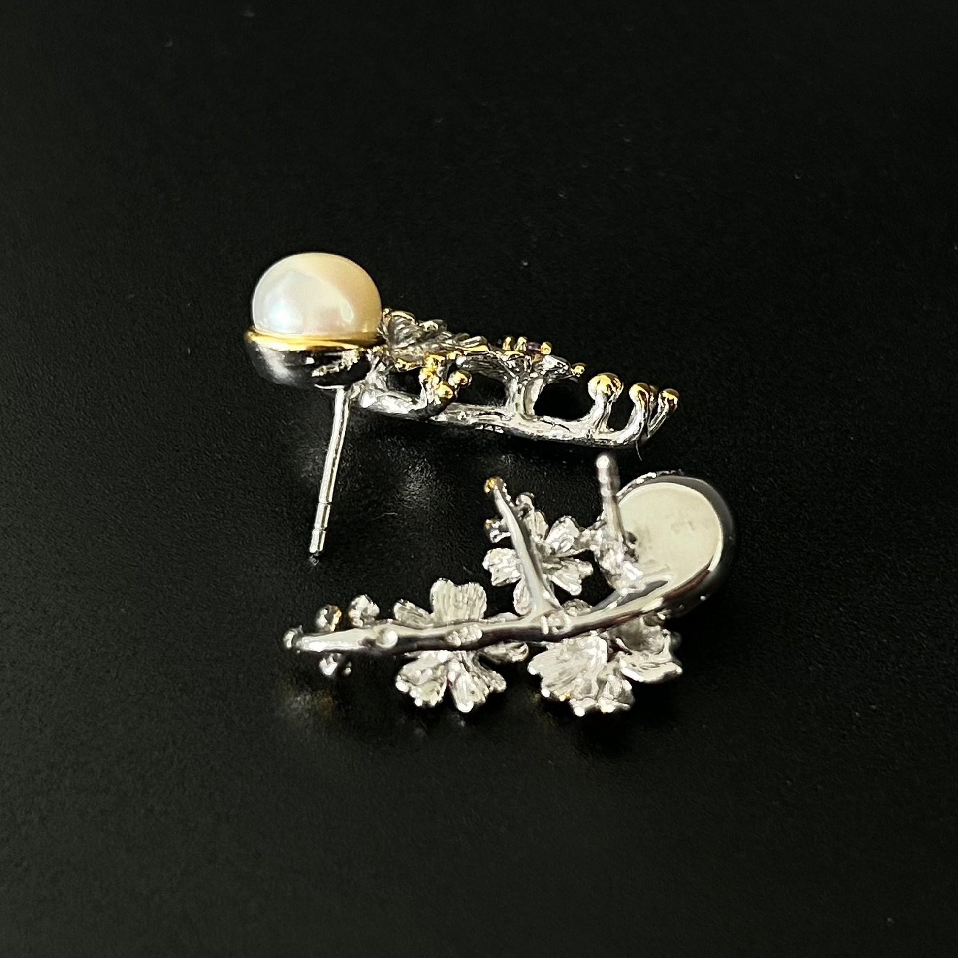 Silver leaf-shaped earring with a pearl on a black background
