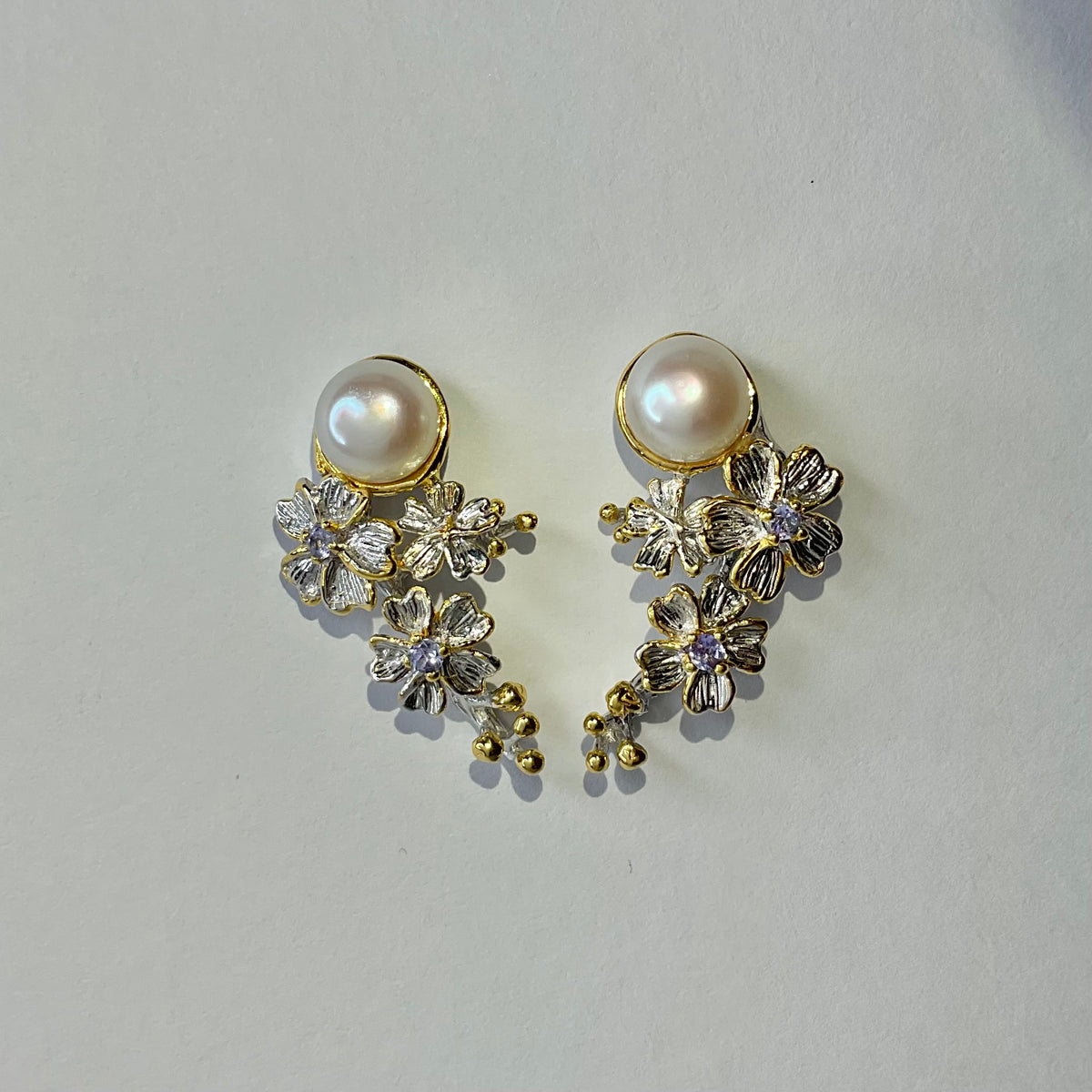 Pair of earrings with pearls and floral designs on a light gray background