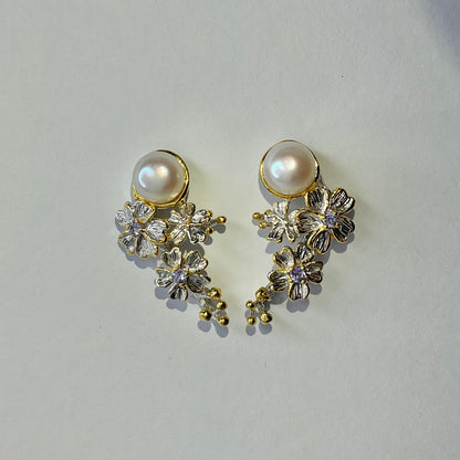 Pair of earrings with pearls and floral designs on a light gray background