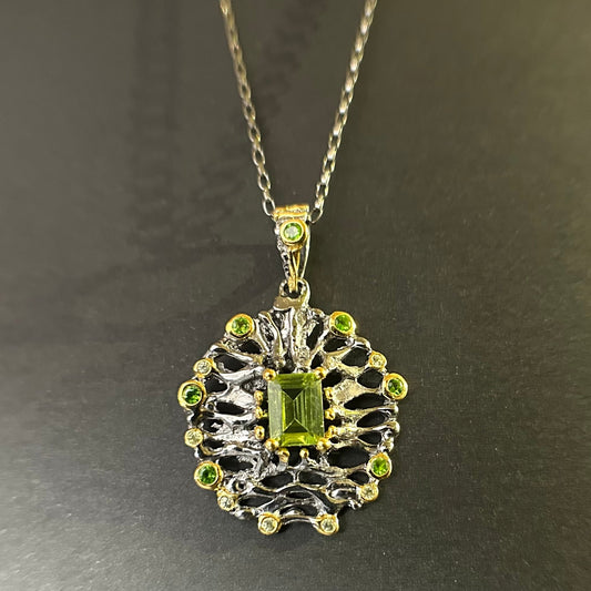 Silver pendant with green gemstones on a chain against a dark background