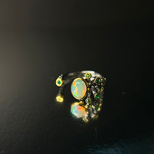 Ring with opal stone and green gemstones on a black background