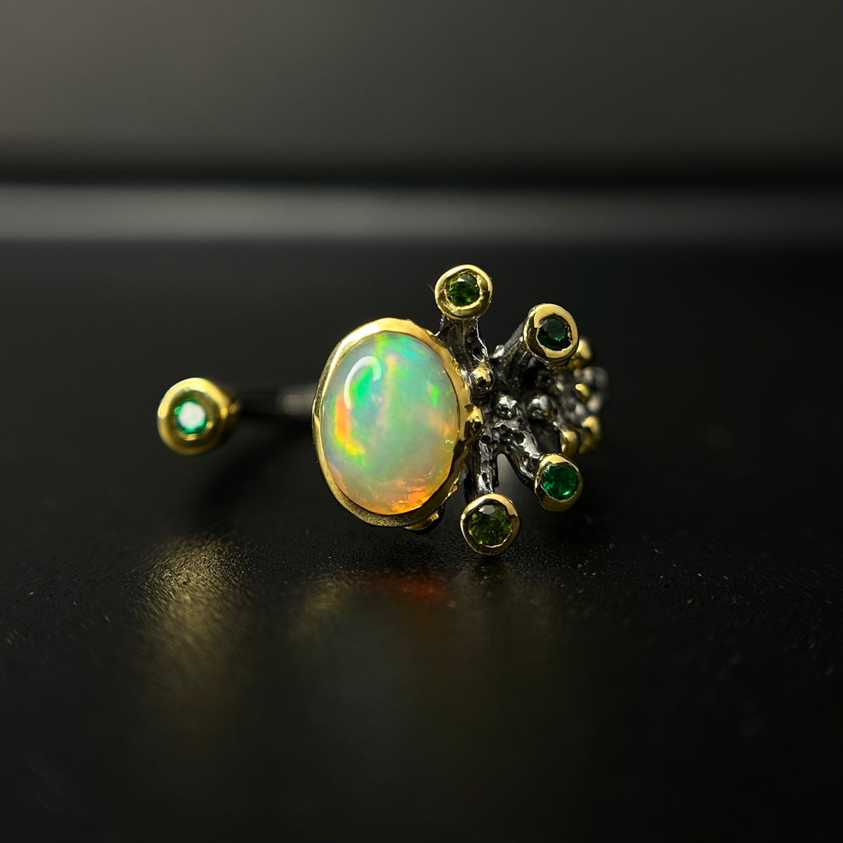 Gold ring with opal and green gemstones on a black background