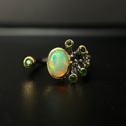 Gold ring with opal and green gemstones on a black background