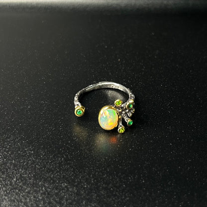 Silver ring with a central opal stone and smaller green stones on a black background