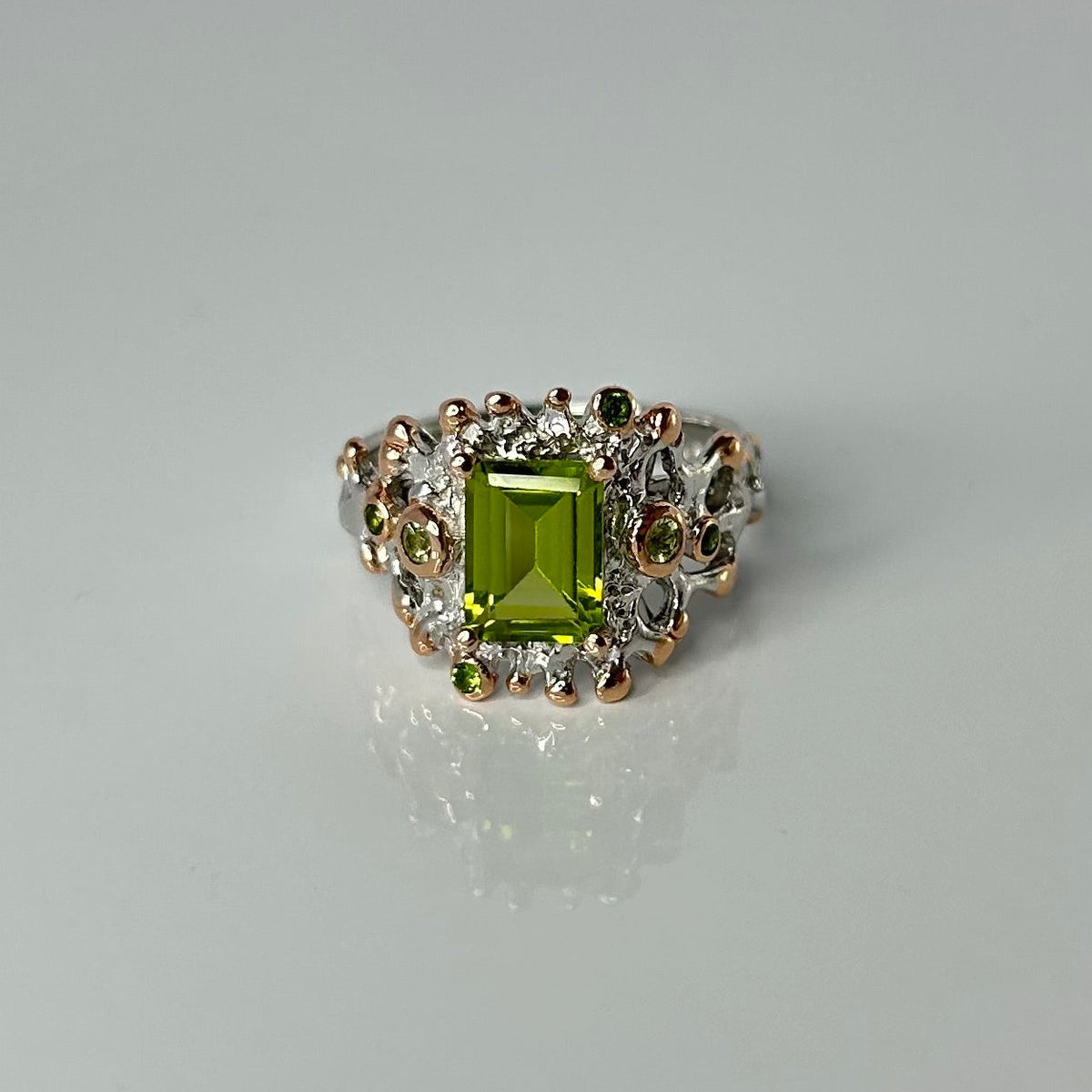 Silver ring with a green peridot gemstone and small accents on a gray background