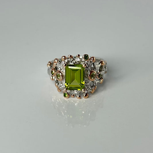 Silver ring with a green peridot gemstone and small accents on a gray background