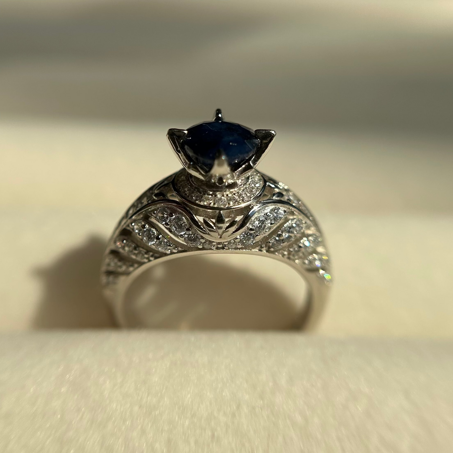 Silver ring with a blue sapphire on a beige background