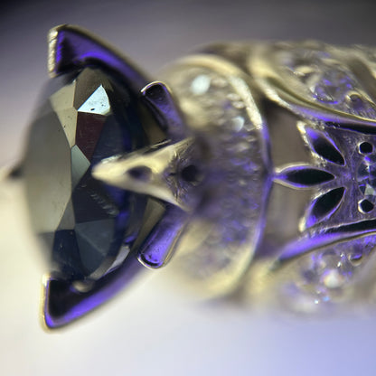 Close-up of a decorative silver ring with intricate designs and a purple sapphire.