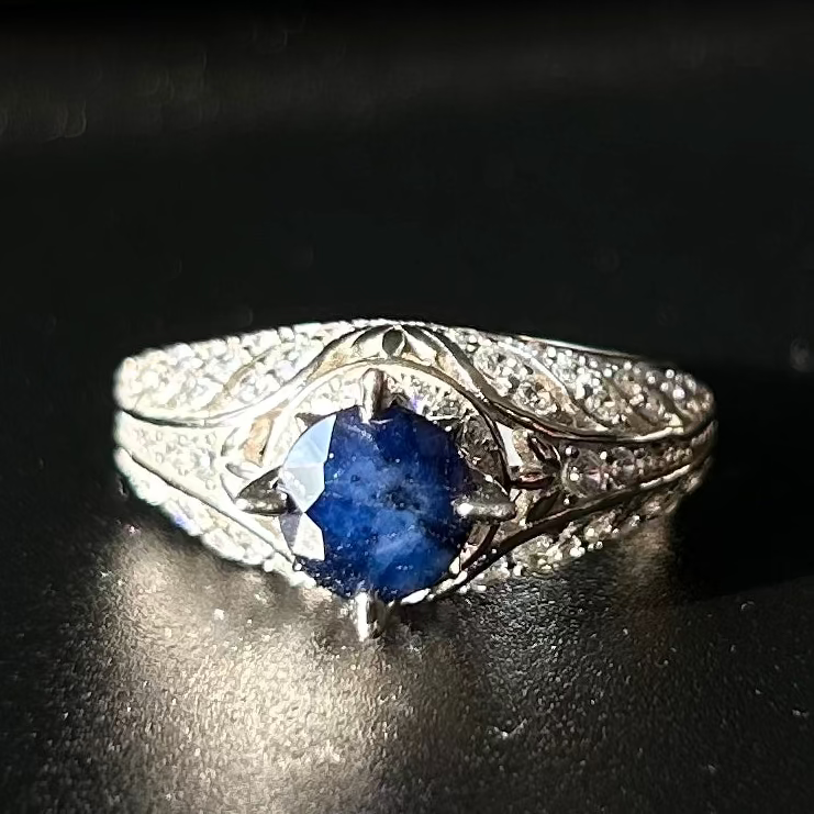 Silver ring with a blue sapphire on a black surface.