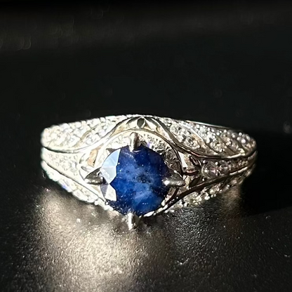 Silver ring with a blue sapphire on a black surface.