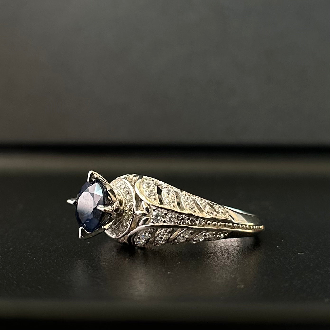 Silver ring with a blue sapphire on a black surface.
