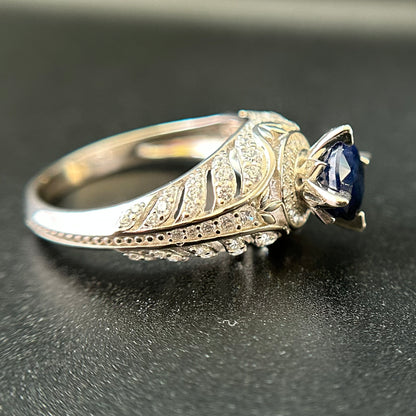 Silver ring with a blue sapphire on a black surface.