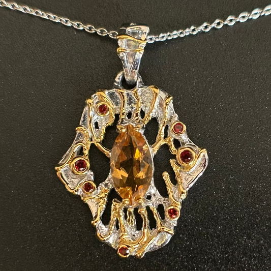 Silver and gold necklace with central Citrine gemstone and red garnet stones on a black background