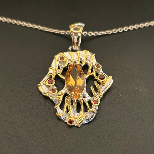 Silver and gold necklace with central Citrine gemstone and red garnet stones on a black background
