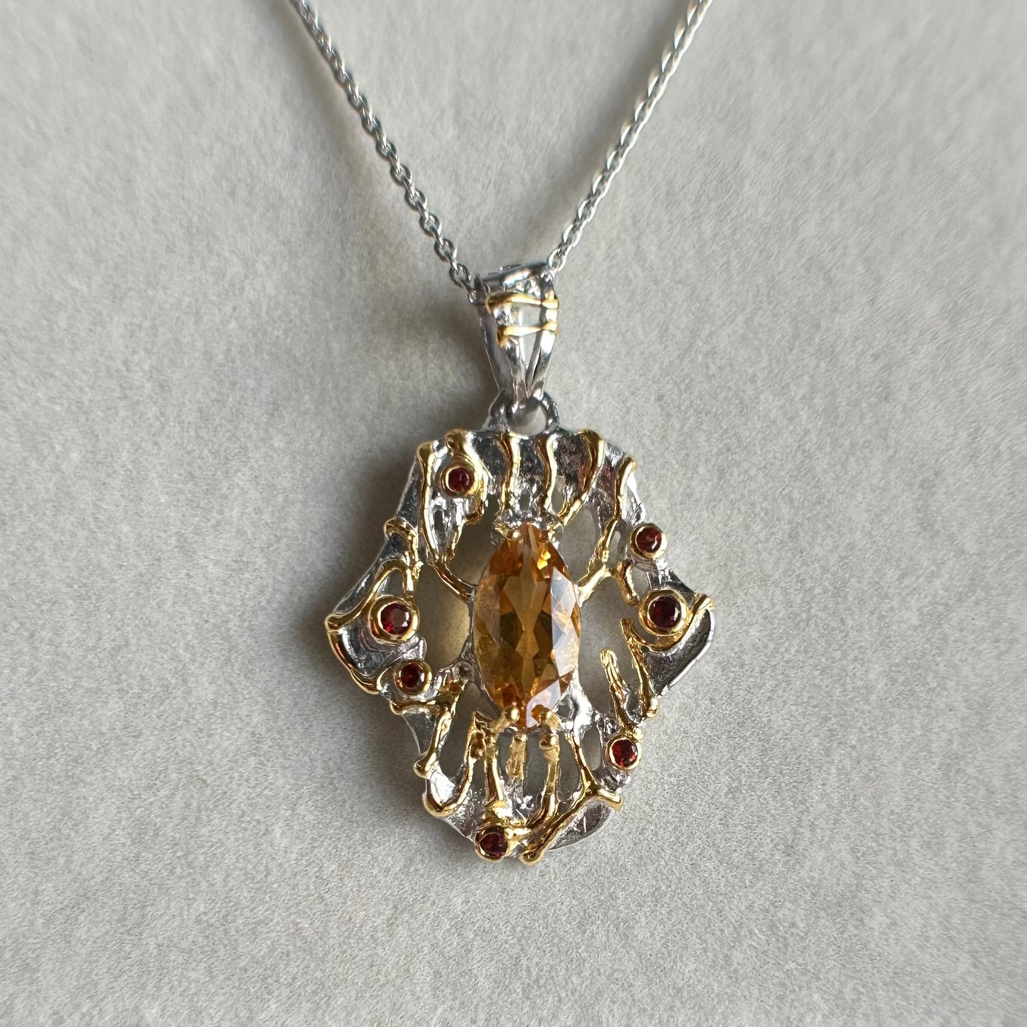 Gold and silver pendant with a central gemstone on a light gray background