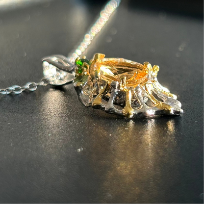 Gold and silver pendant with a green gemstone on a dark surface