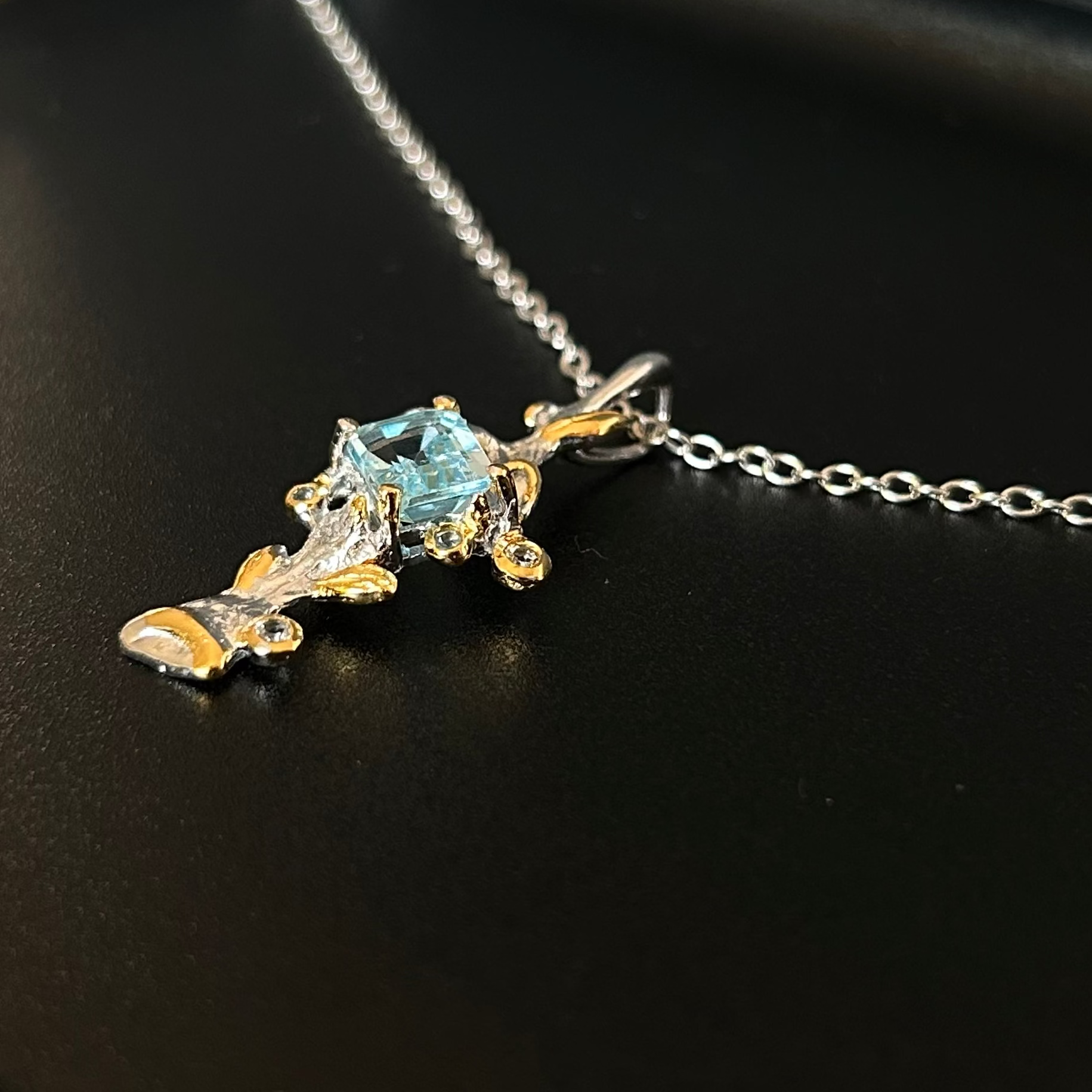Silver pendant with 22k gold plating and a central Topaz on a black background