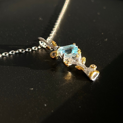 Silver pendant with 22k gold plating and a central Topaz on a black surface