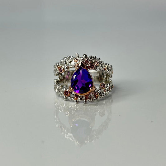 Silver ring with a purple teardrop amethyst gemstone on a light gray background