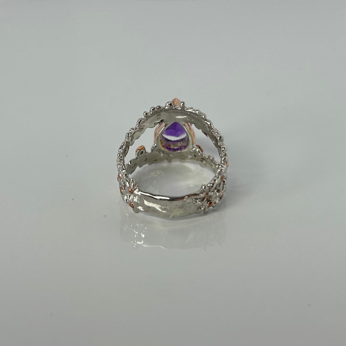Silver ring with a purple teardrop amethyst gemstone on a light gray background