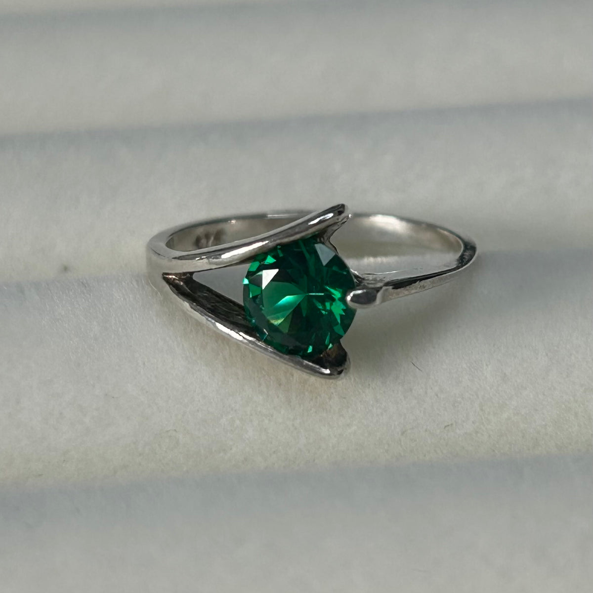 Silver ring with a green gemstone on a light gray background
