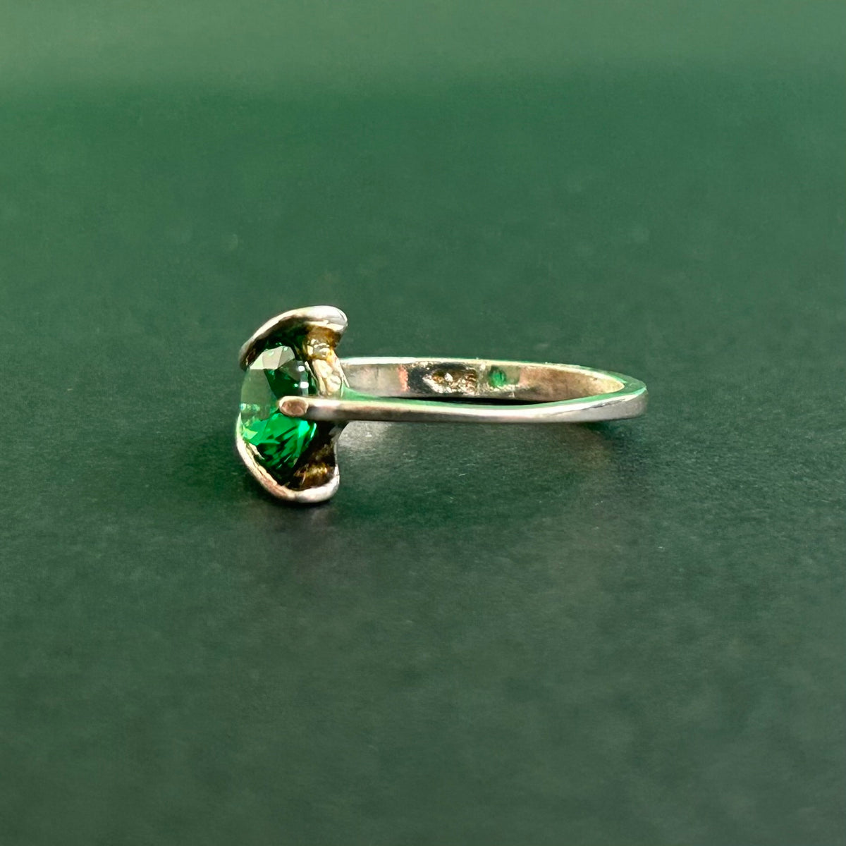 Silver ring with a green gemstone on a dark green background