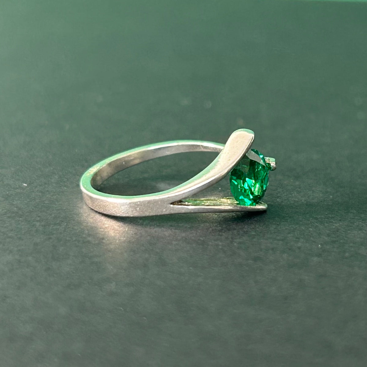 Silver ring with a green gemstone on a dark green background