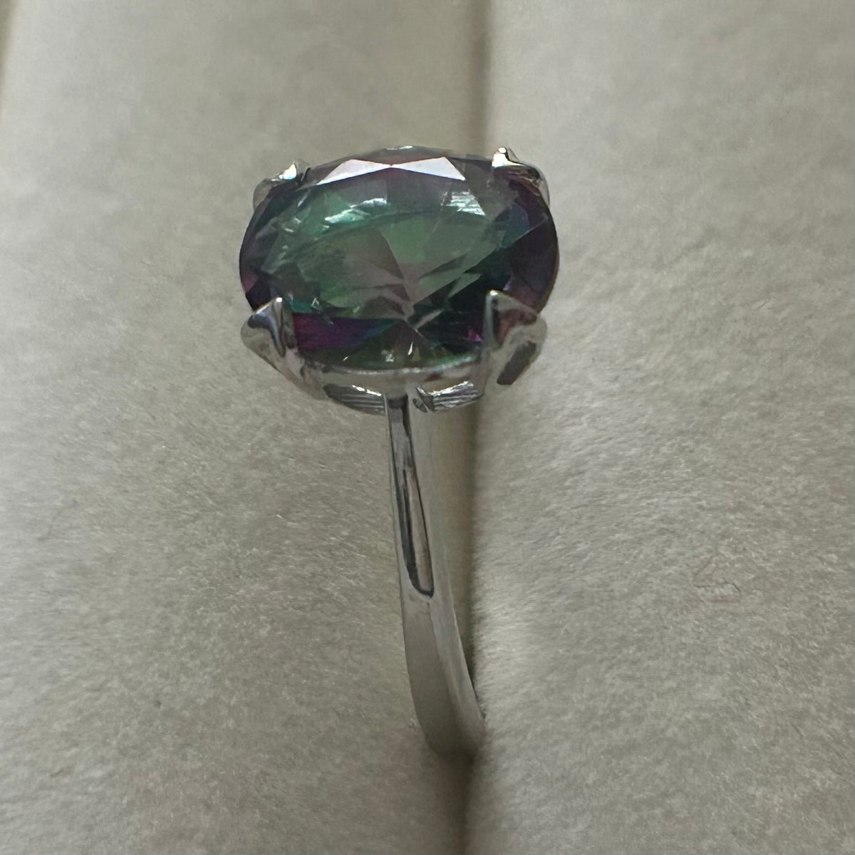 Silver ring with a large, faceted gemstone on a light gray background