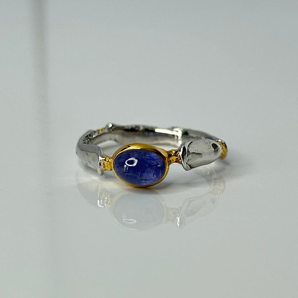 Silver and gold ring with a blue tanzanite gemstone on a light gray background