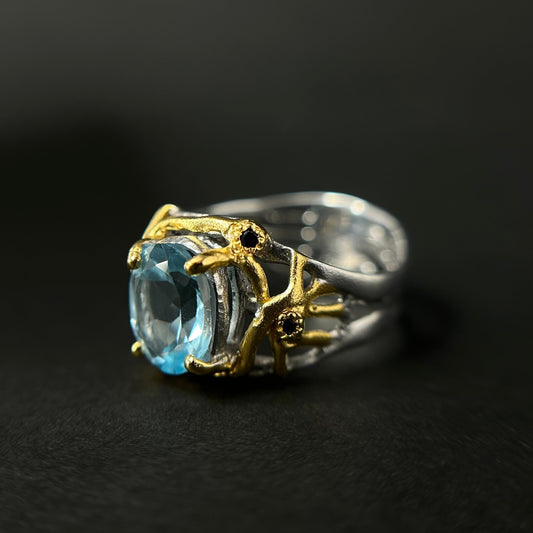 Silver ring with a blue topaz gemstone and gold accents on a dark background