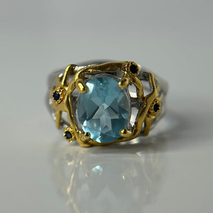 Silver and gold ring with a blue topaz gemstone on a gray background