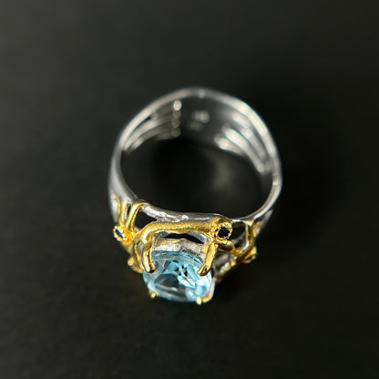 Silver ring with a blue ropaz gemstone and gold accents on a dark background