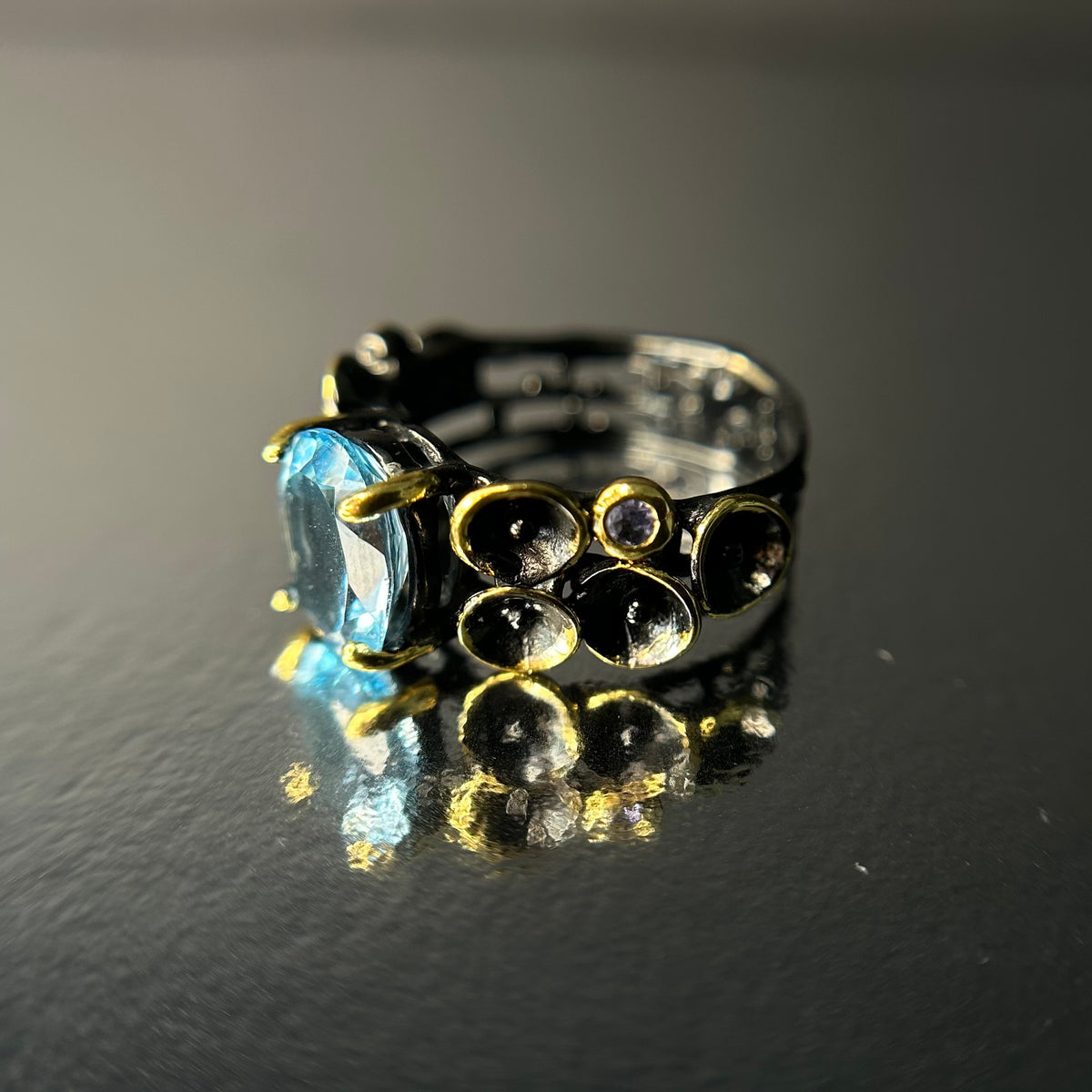 Ring with a blue topaz gemstone and gold accents on a reflective surface