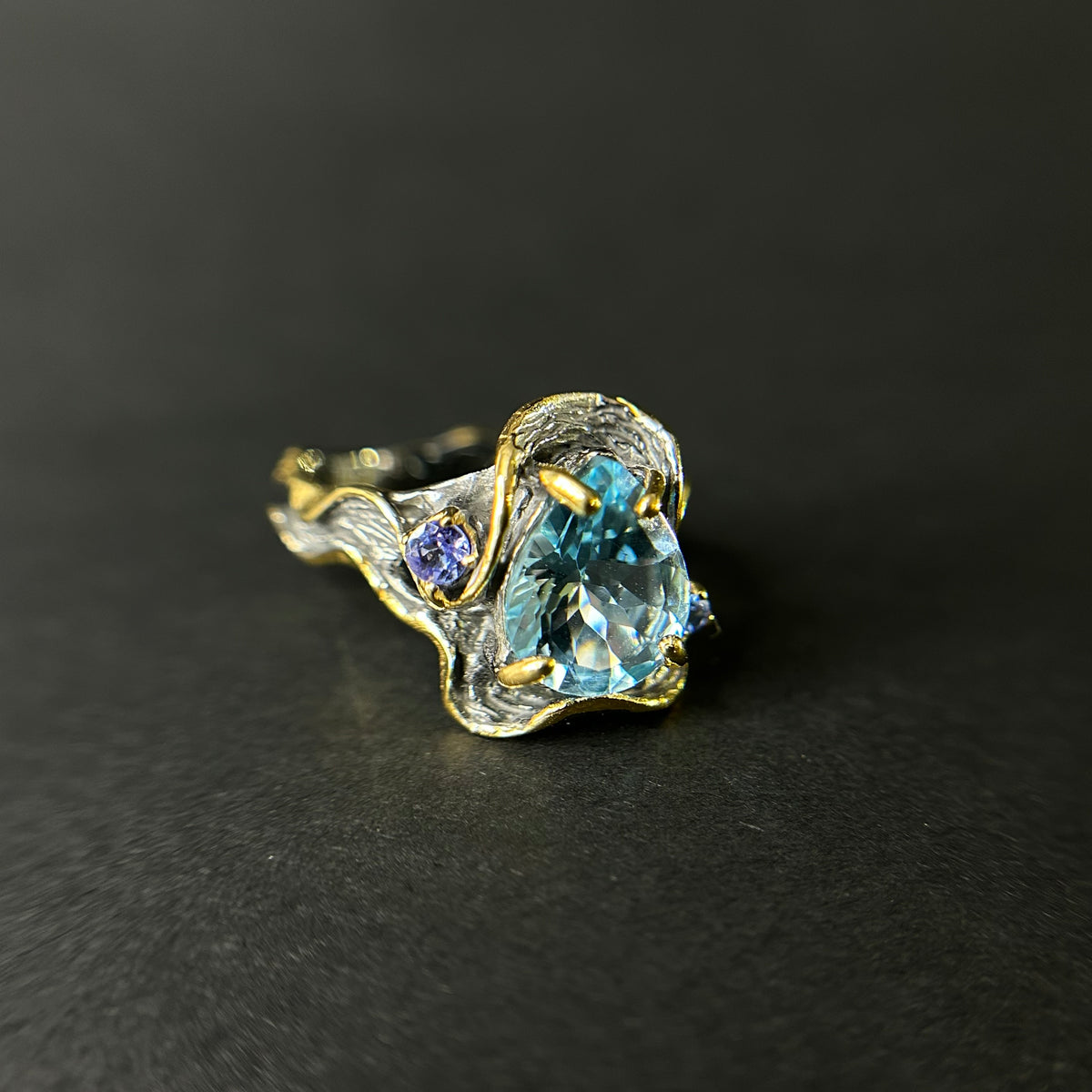 Gold and silver ring with blue topaz gemstone on a black background