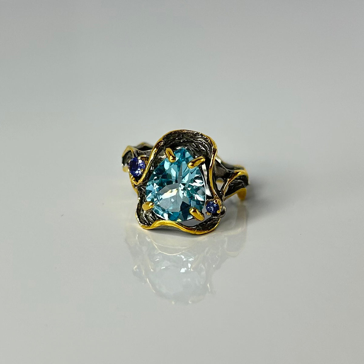 Gold and silver ring with a blue topaz gemstone on a gray background