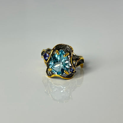 Gold and silver ring with a blue topaz gemstone on a gray background